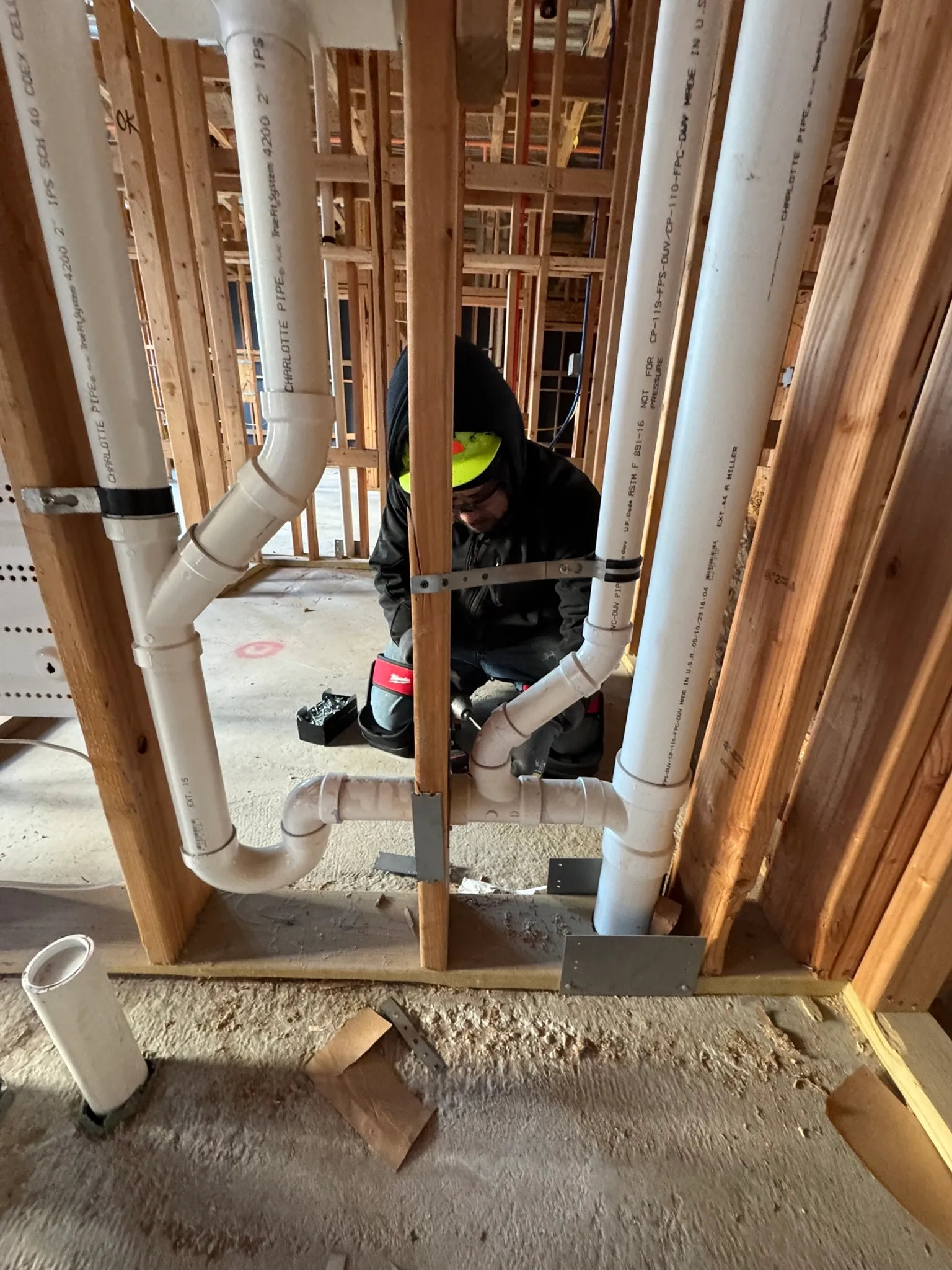 Plumber working on PVC pipe installation in a framed construction site, showcasing precision and craftsmanship in plumbing services.