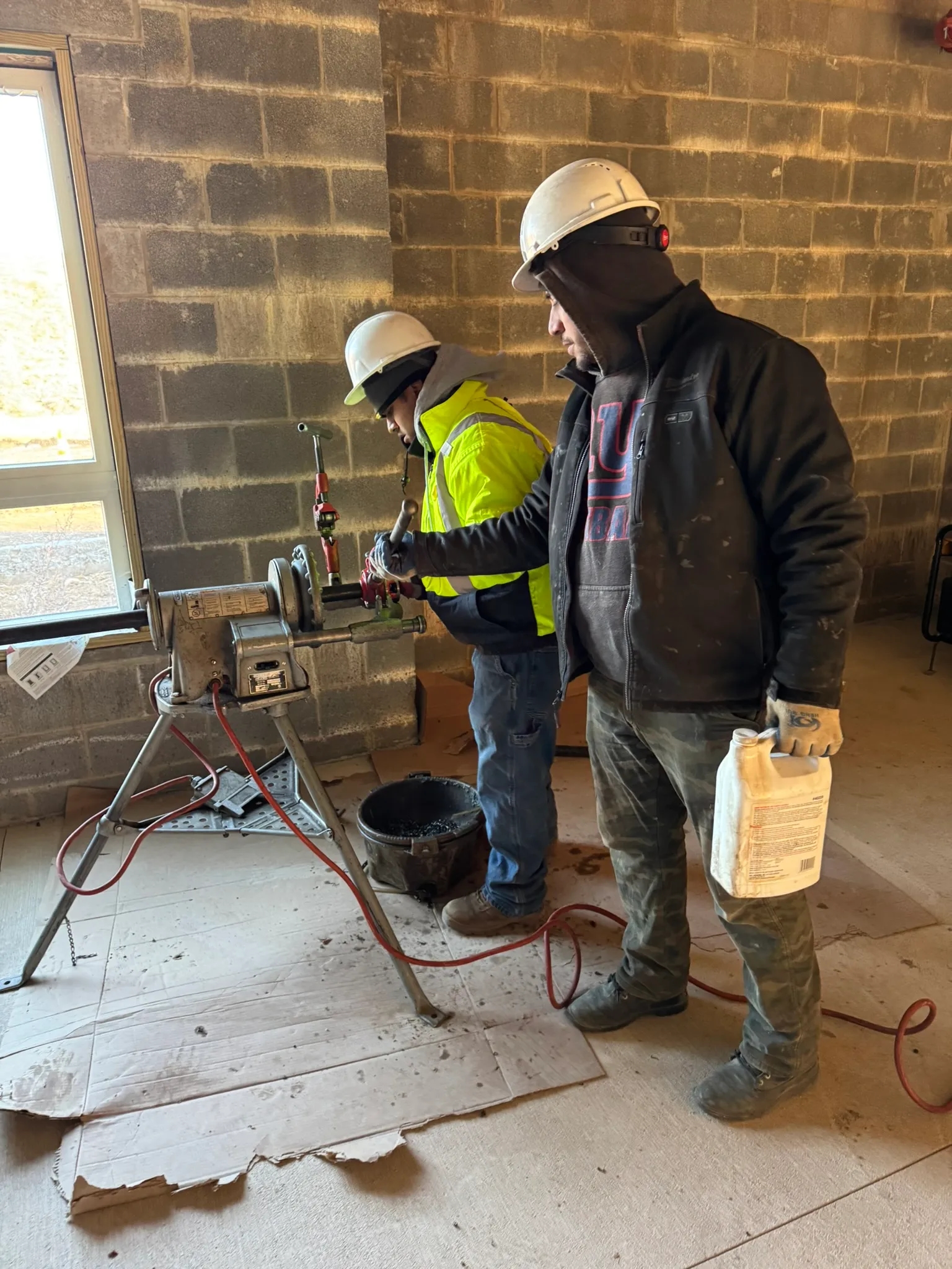 Professional plumbers at a construction site using pipe threading equipment, showcasing expertise and teamwork for plumbing and pipefitting services.