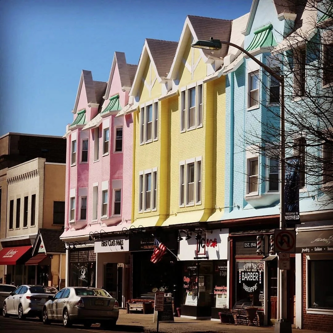 Colorful storefronts and businesses in a vibrant downtown area of Westfield, New Jersey, showcasing local shops and small businesses on a sunny day.